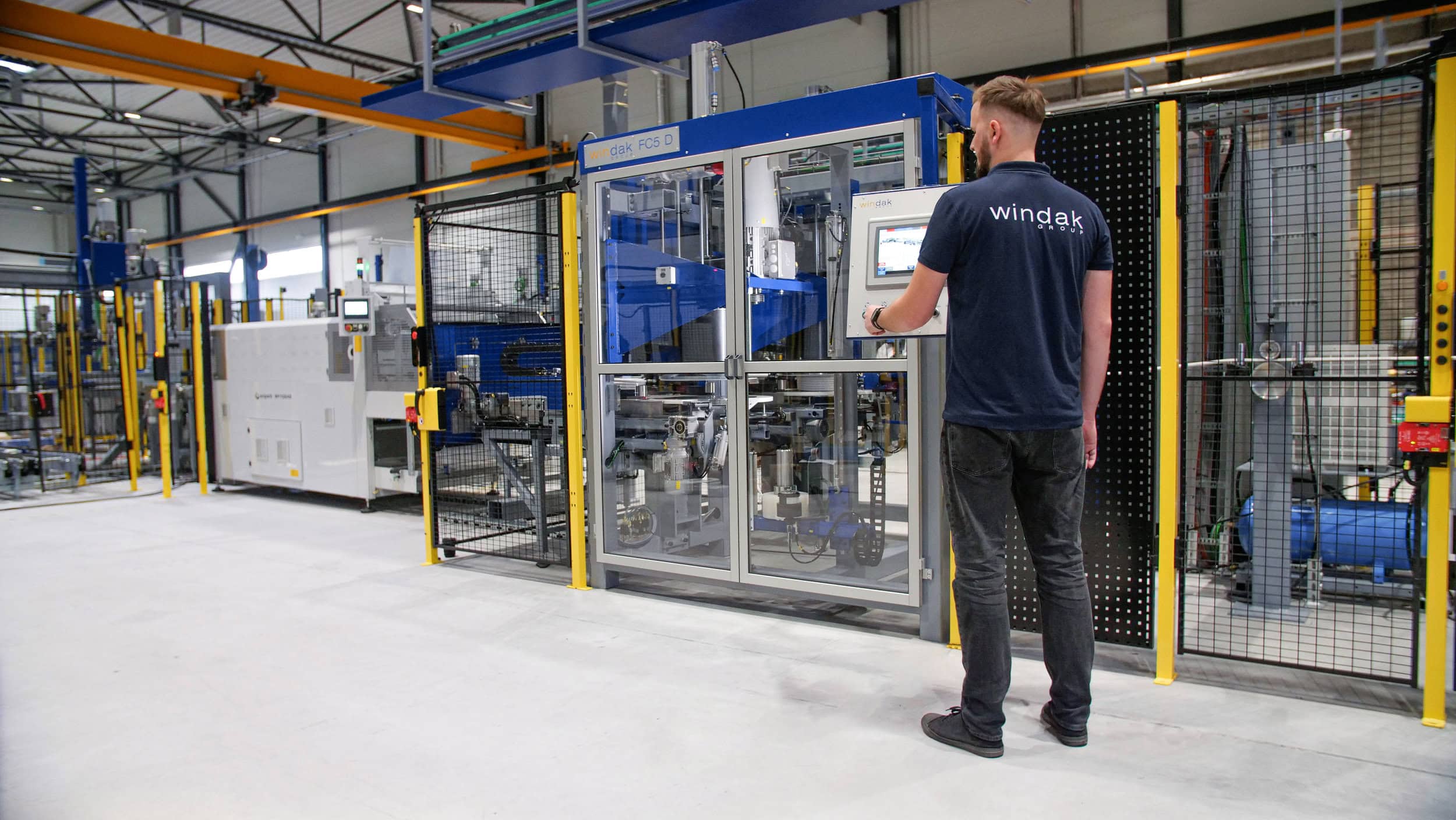 Windak automated cable spooling machine with a technician operating a control panel in a modern industrial setting.