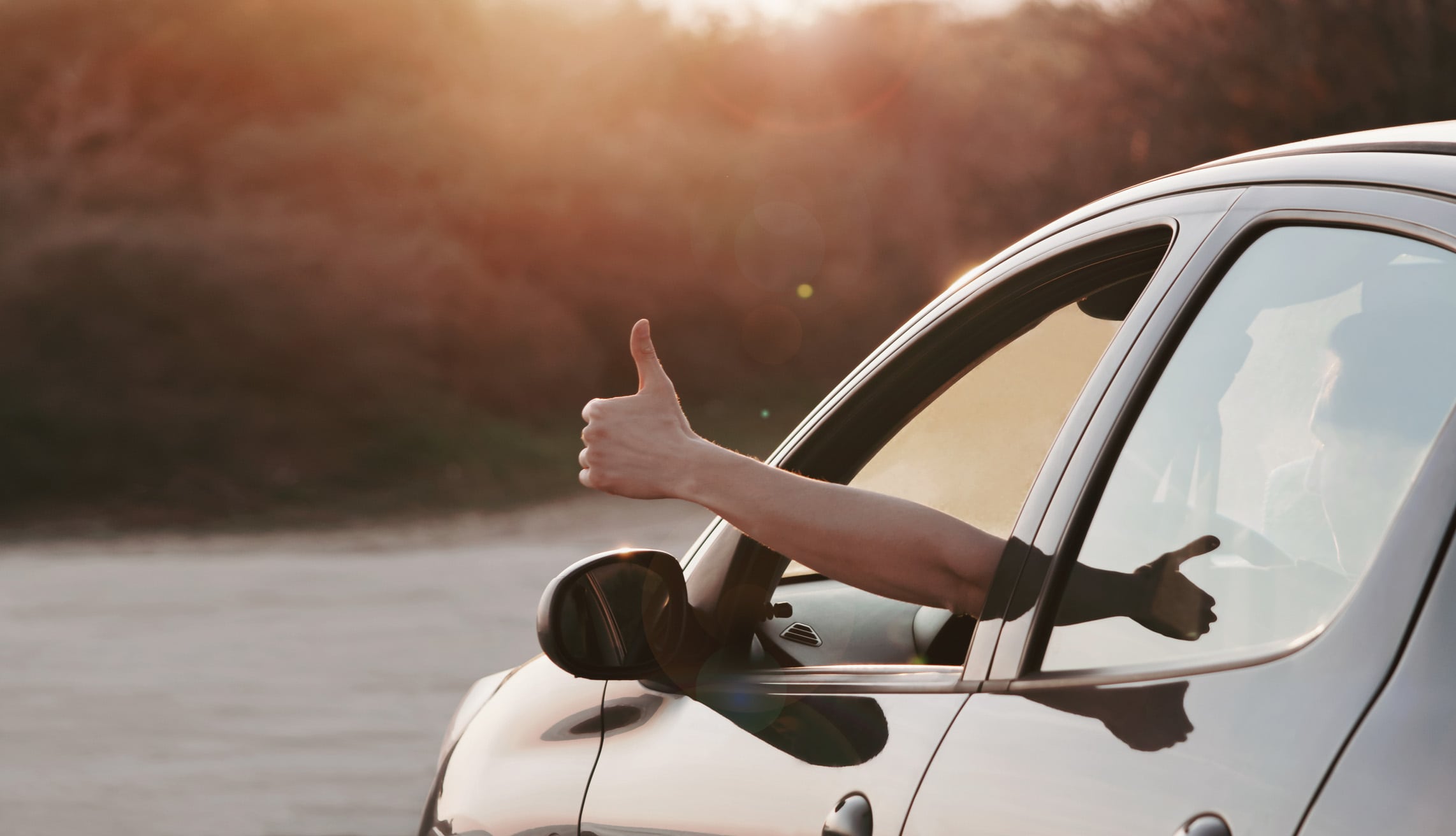 automotive - Man showing thumbs up from car window at sunset